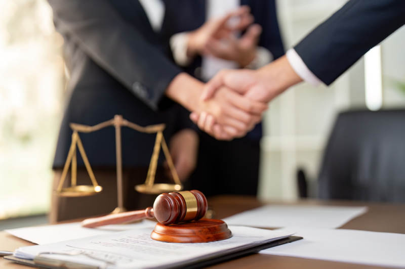 Two people in suits shaking hands over a desk with scales and gavel